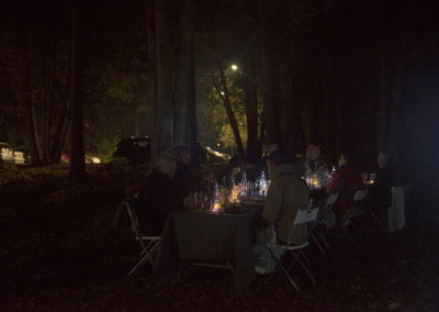 A community meal at a long table surrounded by trees at night